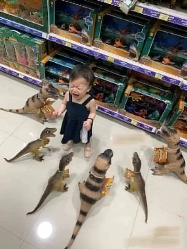 Dieťa v hračkárstve obklopené dinosaurami, vyzerá prekvapene a vystrašene.