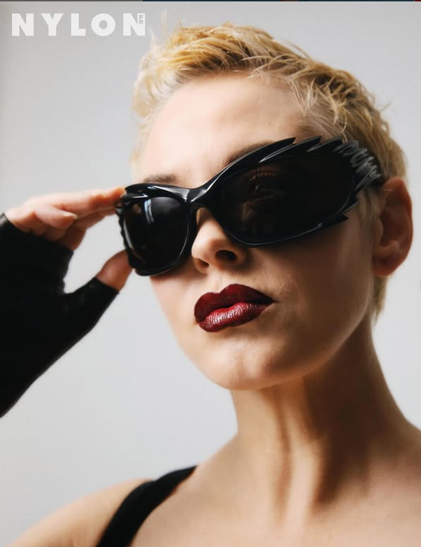 ```plaintextOsoba s krátkymi blond vlasmi a čiernymi okuliarmi pózuje pre módny časopis.
```