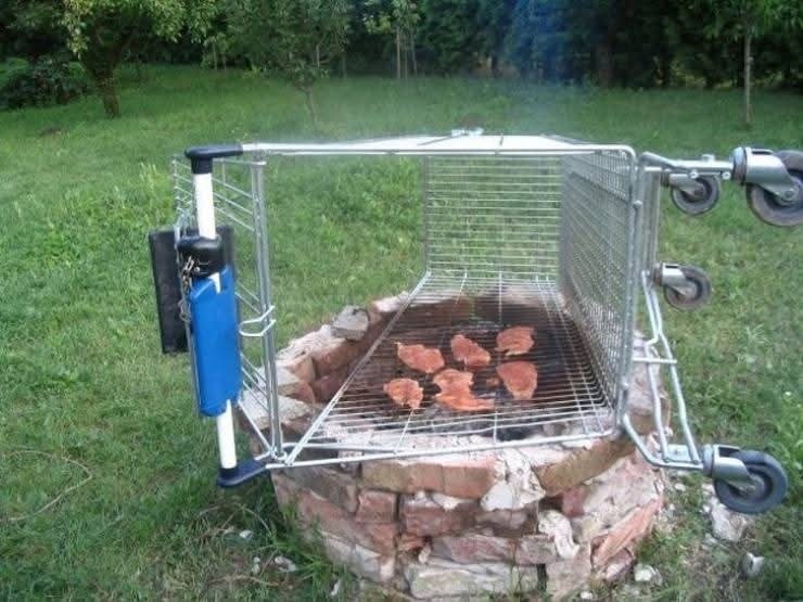 Improvizovaný gril z prevráteného nákupného vozíka s plátkami mäsa na tehálkach v záhrade.