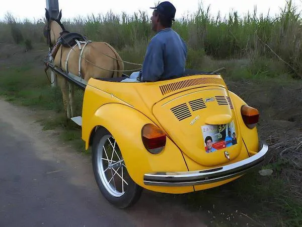 Koňský povoz s retro karosériou vtipného dizajnu, ktorý kombinuje auto a záprah na vidieckej ceste.