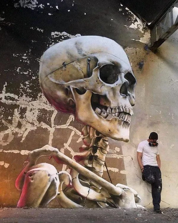 Graffiti obrovská kostra na stene, umelec v maske stojí opretý. Moderné pouličné umenie a kreatívna grafika.