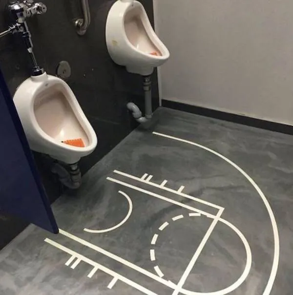 Basketbalové ihrisko na podlahe toalety s dvoma pisoármi pripomína hravé prostredie.