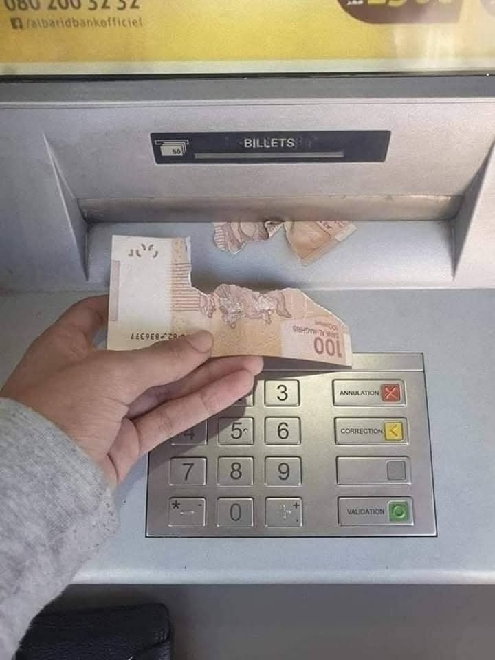 Osoba drží roztrhnutú bankovku pri bankomate, zrejme chyba pri vydávaní hotovosti.