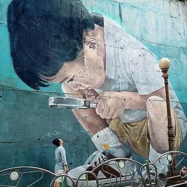 Mural dieťaťa s lupou na stene, mladý muž pod ním obdivujúci umenie.