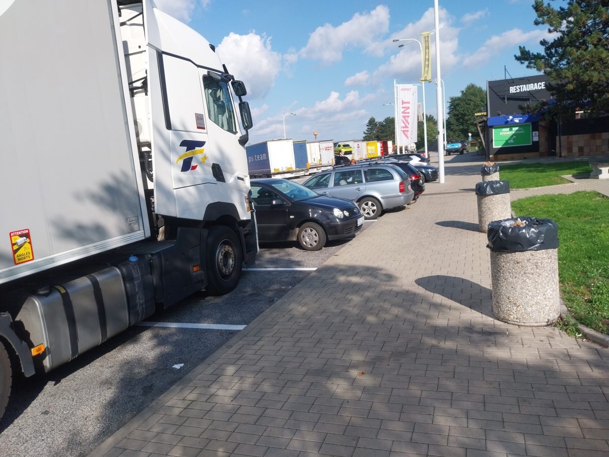 Kamión zaparkovaný na parkovisku vedľa osobných áut, modrá obloha s mrakmi.