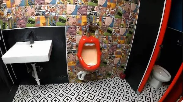 Originálny pisoár v tvare úst na farebnej toalete s geometrickou dlažbou.