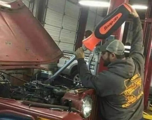 Muž nalieva olej do motora auta pomocou obrovskej lievikovej nádoby v autodielni.