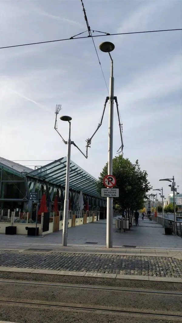 Pohľad na ulicu s kreatívnym verejným umením, lampa s ramenami rozvetvenými na nebe.