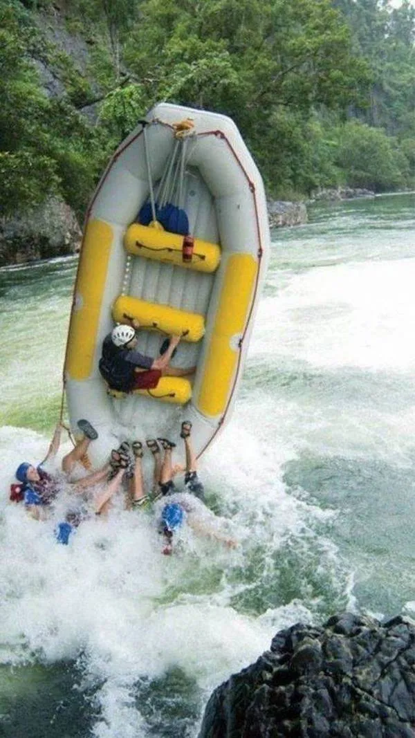 Rafting na divokej rieke: skupina ľudí prevrátená s raftom vo vodnom prúde medzi skalami. Adrenalínový zážitok v prírode.