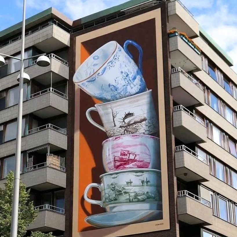 Obrovská nástenná maľba s motívom stohovaných šálok na budove v mestskom prostredí, tvorba urban art.