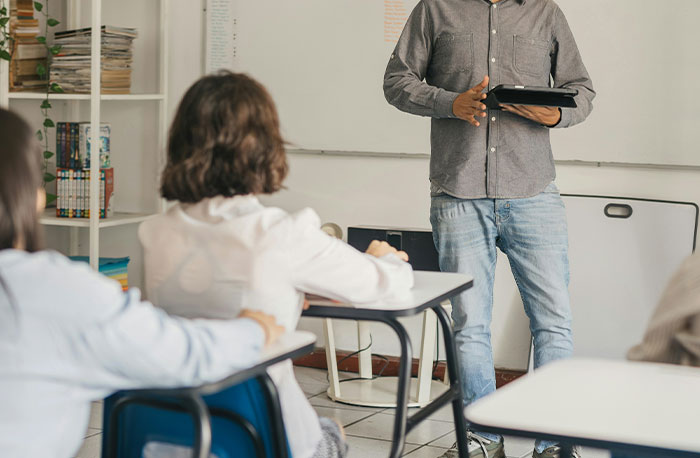 Učiteľ s tabletom prednáša študentom v učebni, zameranie na interakciu a vzdelávacie prostredie.