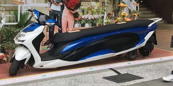 Neobvykle dlhá modro-biela motorka zaparkovaná pred obchodom s kvetmi.