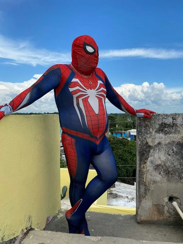 Superhrdina v modro-červenom kostýme stojí na streche s výhľadom na mesto.