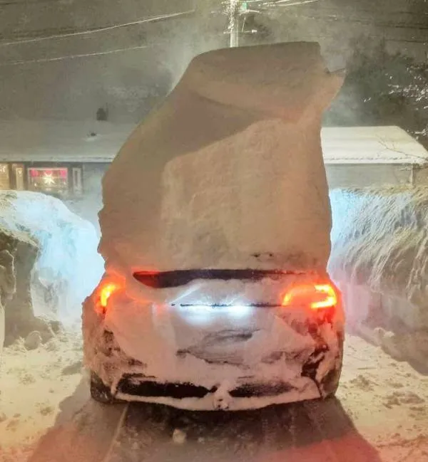 Auto pokryté snehom počas intenzívnej zimnej búrky, so zvýraznenými zadnými svetlami.