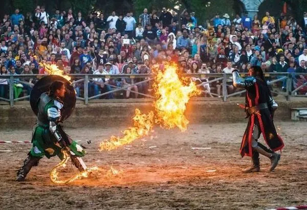 Dvaja rytieri predvádzajú súboj s ohňom počas stredovekého festivalu pred nadšeným publikom.
