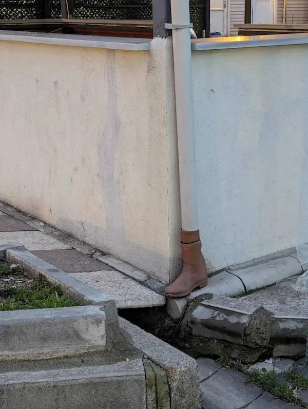 Topánka slúžiaca ako odkvapová rúra pri betónovej stene na nerovnom chodníku.