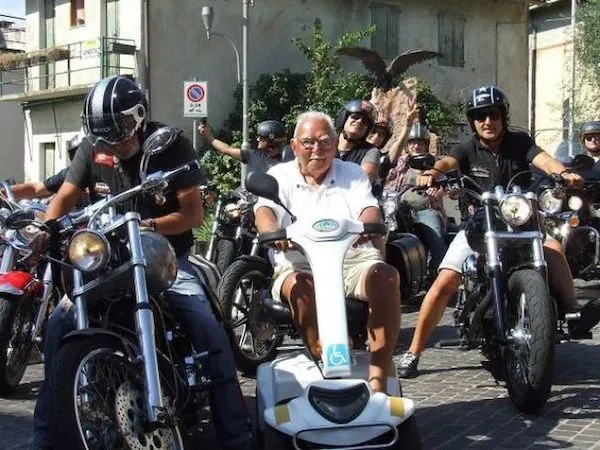 Muž na elektrickom skútri vedie skupinu motorkárov na ulici v meste.
