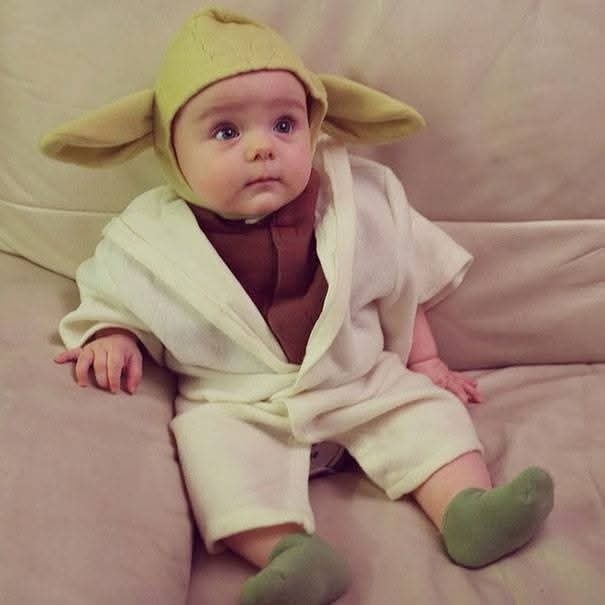 Dieťa v roztomilom kostýme s ušami na pohovke, štylizované ako Yoda zo Star Wars.
