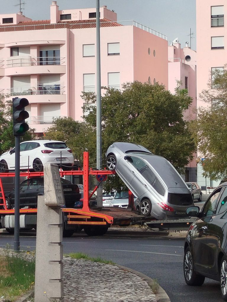 Autotransportér s autami na rušnej križovatke v mestskom prostredí s ružovými budovami.