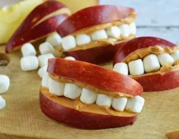 Jablkové snacky s marshmallow a arašidovým maslom v tvare úsmevu na drevenom podnose. Kreatívna zdravá pochúťka.