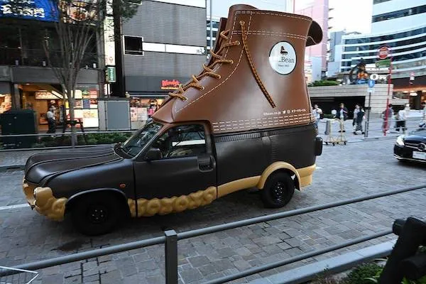 Netypické auto v tvare veľkej topánky jazdí ulicami mesta, pútajúce pozornosť okoloidúcich.