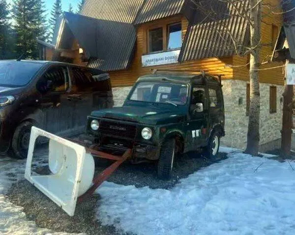Malé terénne auto s originálnou snehovou radlicou na odpratávanie snehu pred dreveným domom.