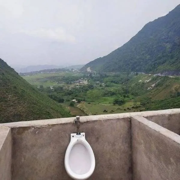 Vonku umiestnený pisoár s výhľadom na zelené údolie a hory.