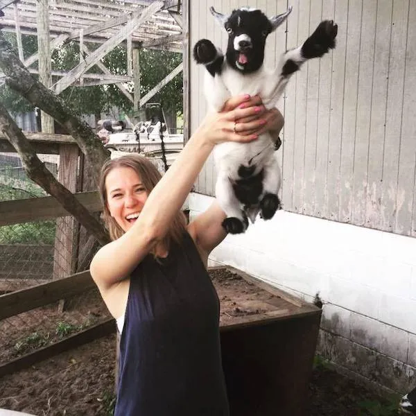 Usmievajúca sa žena drží malé kozliatko vo vzduchu na farme.