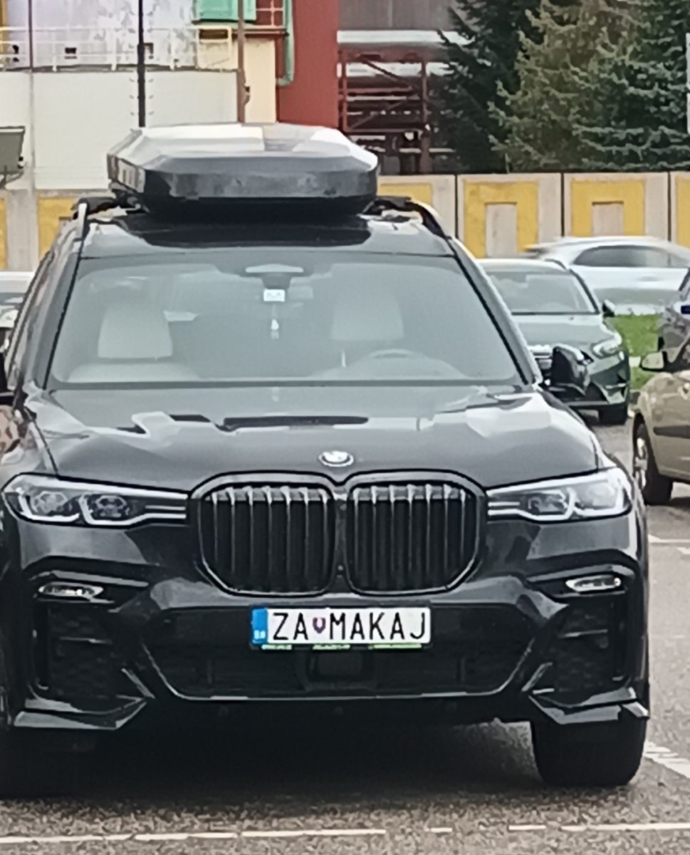 Luxusné BMW SUV s osobitnou ŠPZ „ZAMAKAJ“ na parkovisku, označujúce jedinečný štýl a ašpirácie majiteľa.