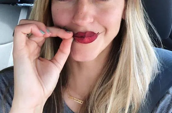 Žena s vtipne tvarovanými perami do úsmevu sedí v aute a usmieva sa.