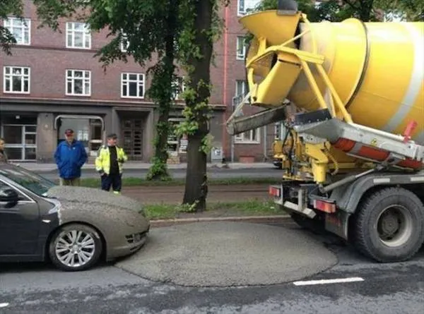 Betónová miešačka vyliala betón na zaparkované auto na ceste, dvaja ľudia sledujú situáciu.