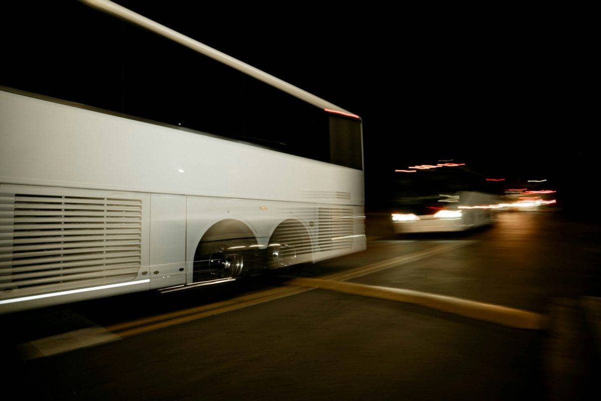 A white bus driving down a street at night