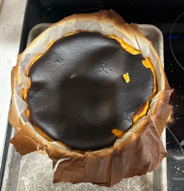 Spálený koláčik v okrúhlej forme na pečenie s tmavou, zapečenou korunkou na vrchole.