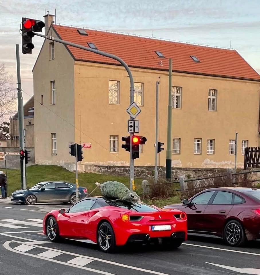 Červené športové auto so stromčekom na streche stojí na červenej na križovatke v meste.