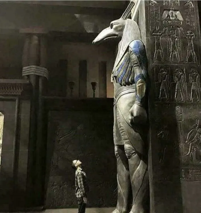 Osoba obdivuje veľkú sochu staroegyptského boha so zvieracou hlavou v historickom chráme.