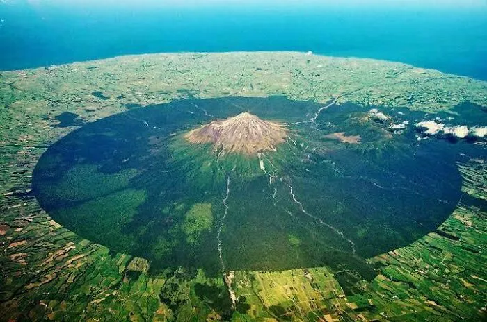 Letecký pohľad na sopku Taranaki obklopenú súvislým lesom na Novom Zélande, vytvára jedinečný kruhový vzor na krajine.