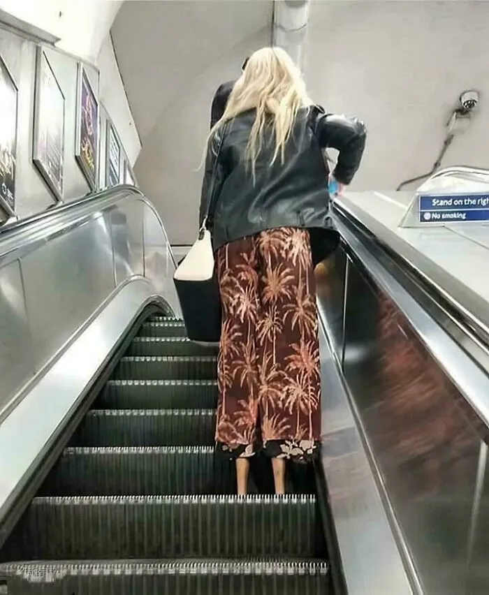 Žena s dlhými nohavicami na eskalátore, módny výzor v mestskej stanici metra.