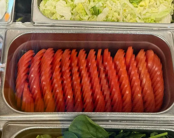 Nakrájané kolieska paradajok úhľadne poukladané v nerezovej gastronádobe na prípravu šalátov.