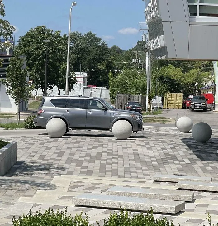 Auto opticky posadené na veľké kamenné gule v modernom mestskom prostredí.
