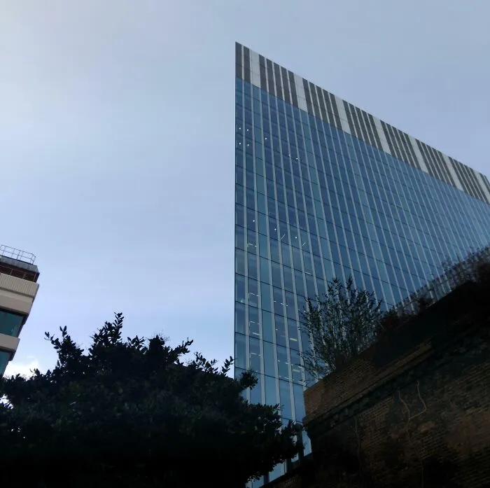 Moderná sklená budova s ostrým rohom a modrým nebom v pozadí. Architektúra a mestské prostredie.