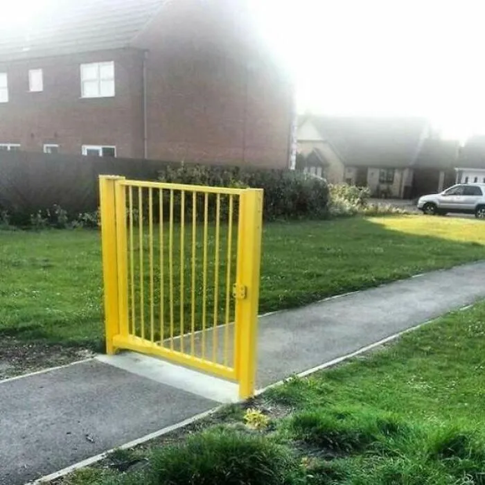 Žltá brána na chodníku bez plota v predmestskej oblasti, symbolický dizajn bez funkčnej bariéry.