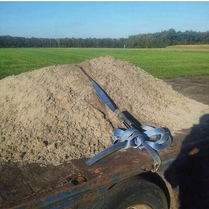 Veľká kopa piesku na prívesnom vozíku so zaistením pomocou modrého popruhu na vidieckom pozadí.
