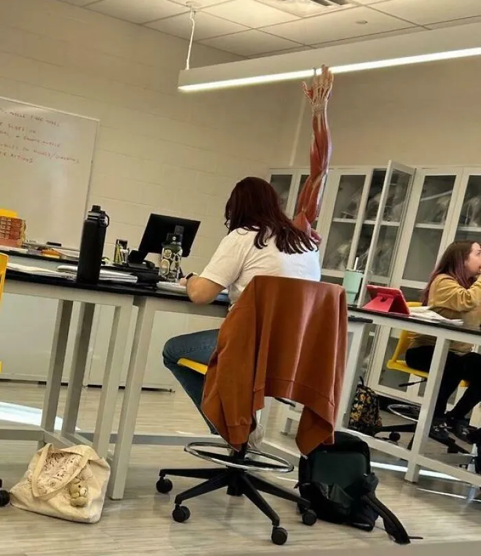 Študentka sedí v laboratóriu, za ňou model ľudskej ruky. Aktívna výučba v triede biológie.