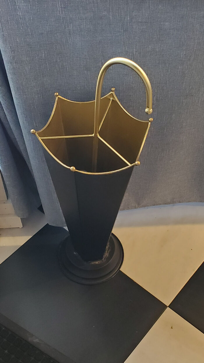 Elegantný stojan na dáždniky v tvare zlatého dáždnika, umiestnený na šachovnicovej podlahe.