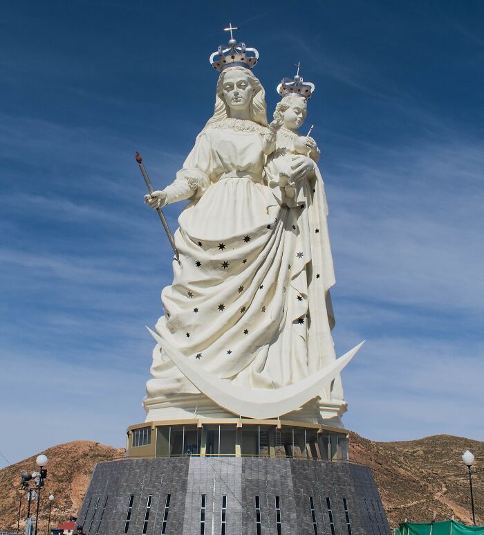 Socha Panny Márie s dieťaťom a korunou na modrej oblohe, monument s hviezdami a mesiacom.