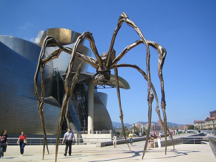 Socha pavúka pri Guggenheimovom múzeu v Bilbau, modrá obloha, turisti sa prechádzajú okolo.