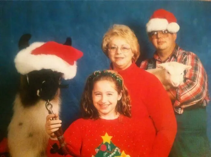 Rodina vianočne oblečená s lamou a kozou, všetci majú na hlave čiapky Santa Clausa.