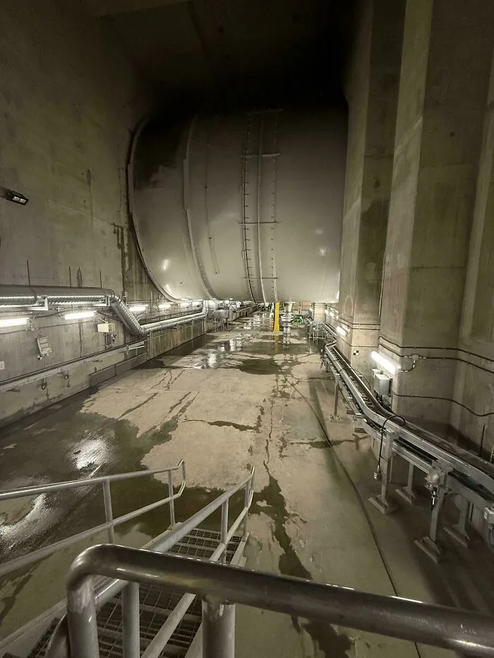 Podzemný tunel s gigantickým valcom, priemyselné potrubia a schodisko do útrob modernej infraštruktúry.