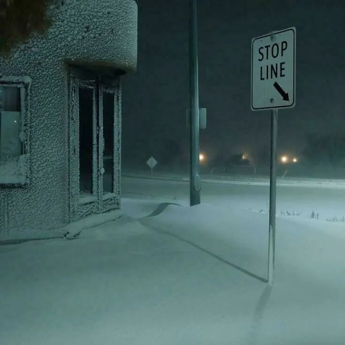 Nočná zimná krajina, zamrznutá budova pri ceste pokrytej snehom, s dopravnou značkou STOP LINE.