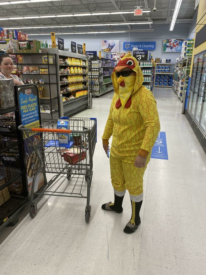 Osoba v kostýme kuriatka nakupuje v supermarkete, tlačí vozík s potravinami.